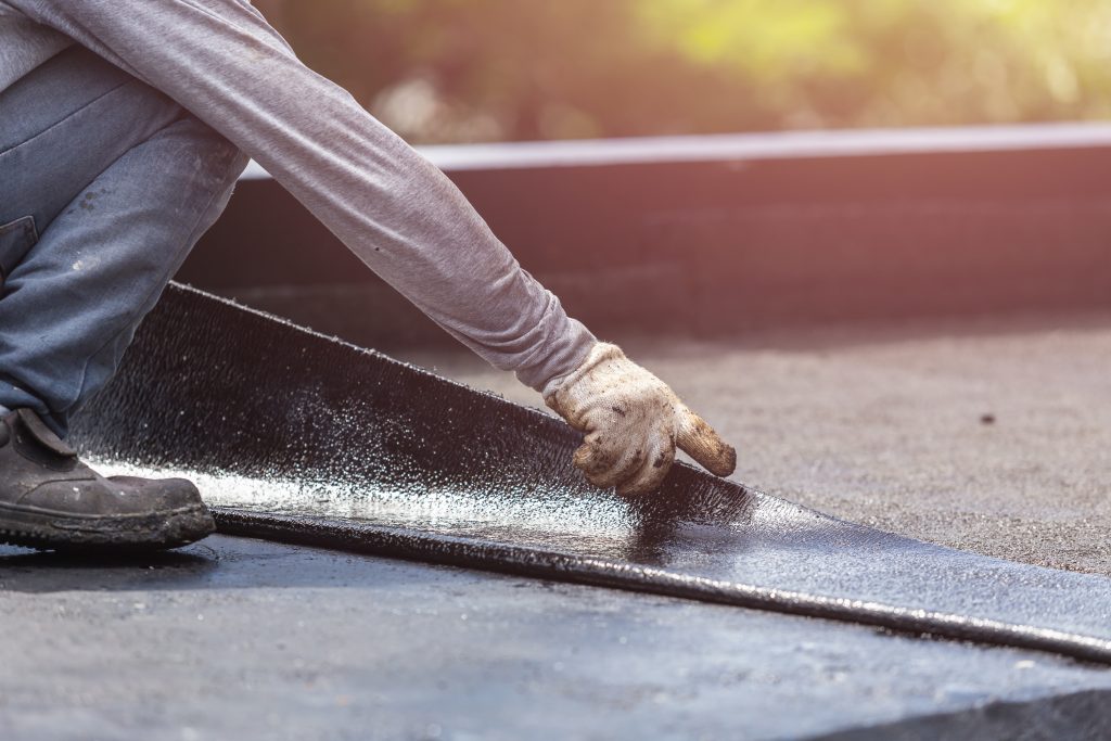 Worker installing tar foil on the rooftop of building. Waterproof system by gas and fire torching